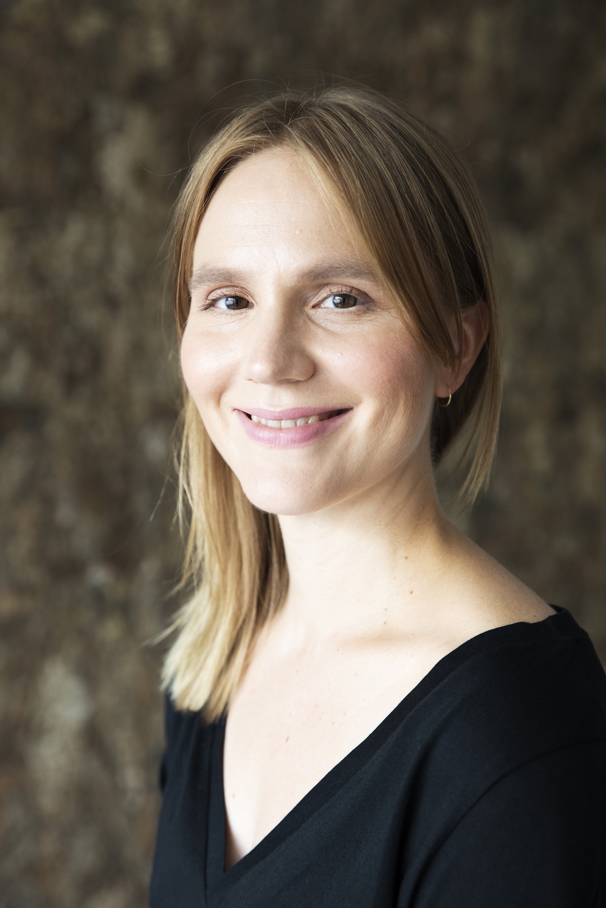 Hymyilevä Anne Pajunen lähikuvassa, musta paita ja pehmeä tausta.
