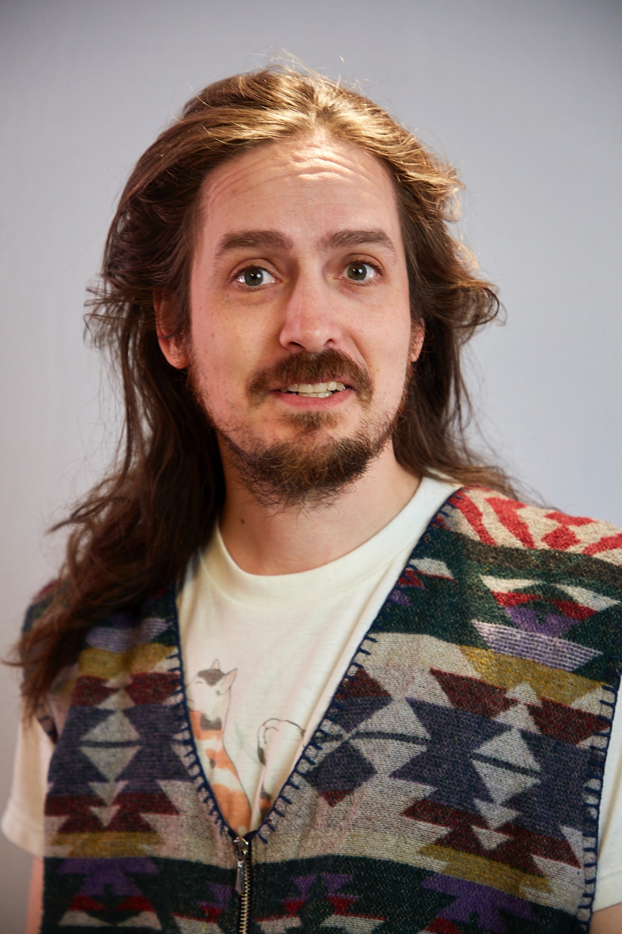 Hymyilevä Sebastian Lopez-Lehto kuvassa, jolla on pitkät tummat hiukset ja parta. Yllään hänellä on kuvioitu neule ja vaalea t-paita.
